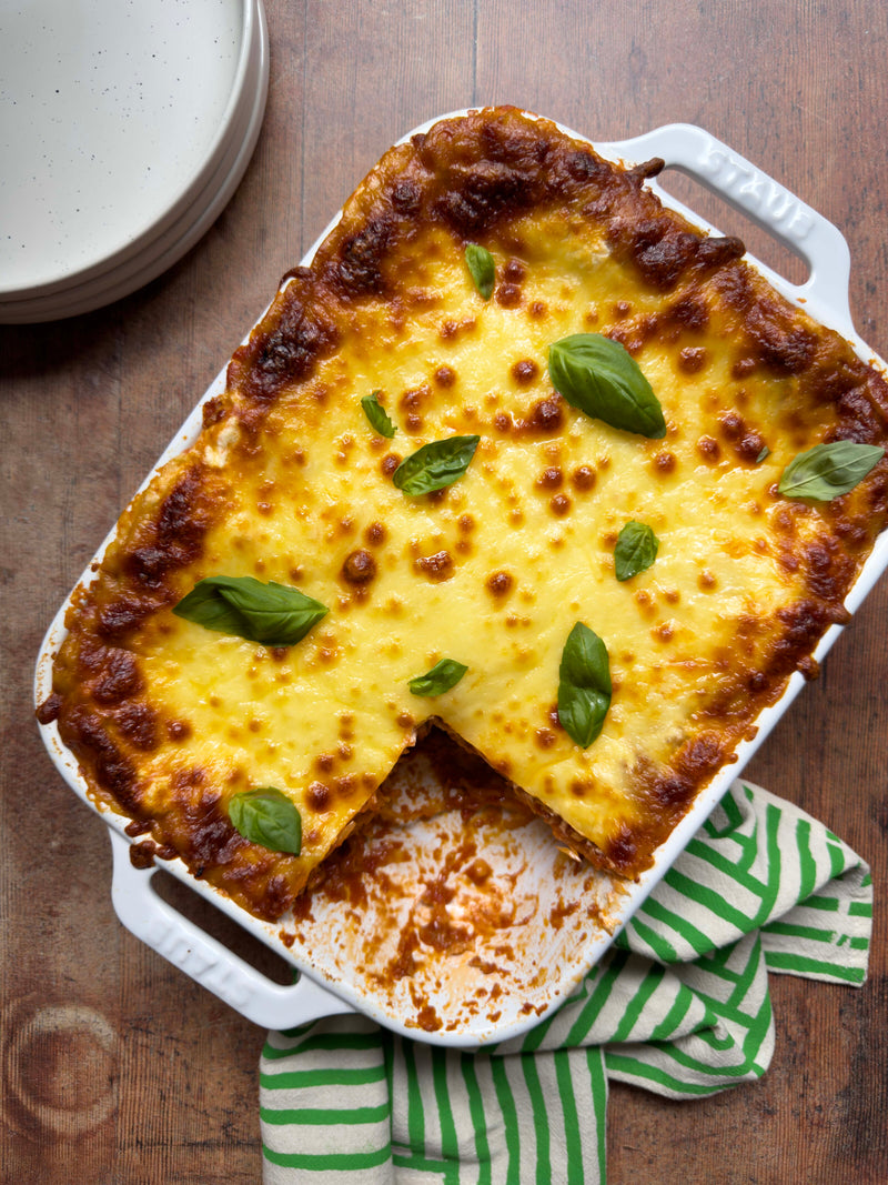 Baked lasagne topped with melted cheese and fresh basil in a white dish