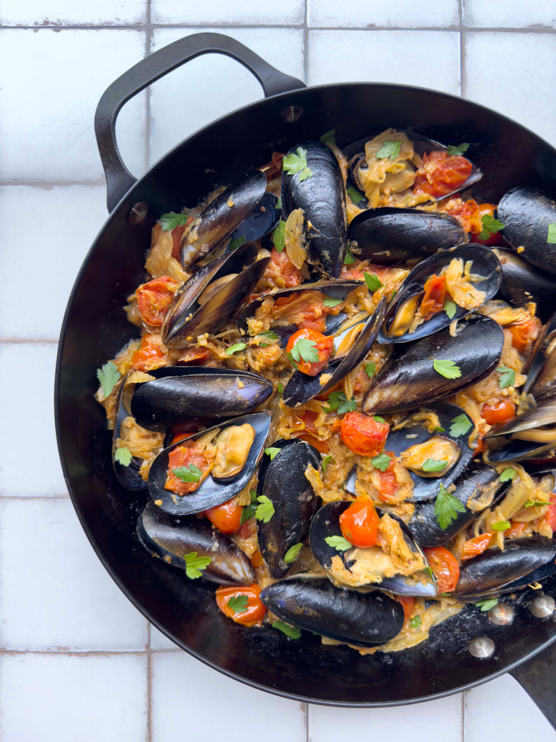 Mussels in a tomato and herb broth, cooked in a cast iron pan